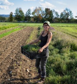 Seven Moon Farm A farmer smiling in the field holding a crate of vegetables