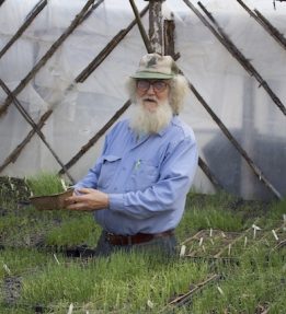 Snakeroot Farmer standing in a greenhouse holding onion seedlings.