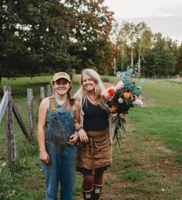 Winterberry Farm Two farmers at Winterberry Farm stand on a green field. One holds an autumnal bouquet of eucalyptus and dahlias.